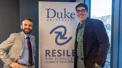two men stand in front of sign reading Duke RESILE