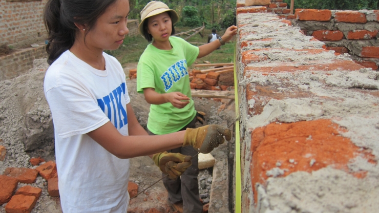 Duke students lay bricks in a wall under construction