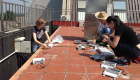 Three students sit on a tiled rooftop working on electronics 