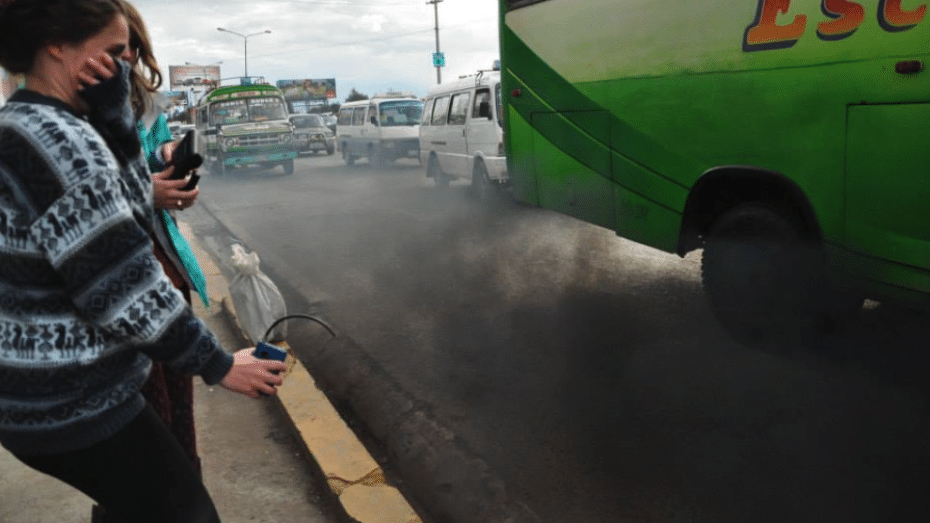 a city bus spews exhaust while a person holds out an air pollution sensor