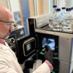 man in lab coat holding vials next to a machine